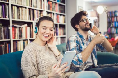 Dijital tablet kullanarak, müzik dinlemek ve smartphone tarafından kafede kapalı konuşmak genç Çift 