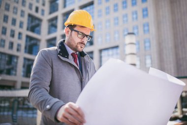 Koruyucu kask holding blueprint ofis binası önünde mimar