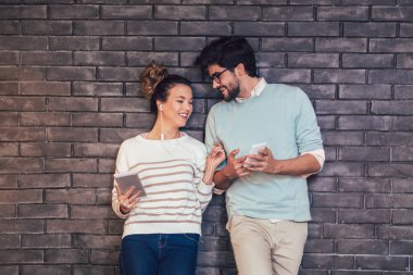 Tablet ve smartphone üzerinde tuğla duvar arka plan kullanarak mutlu genç Çift