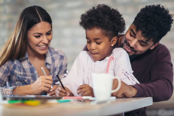 Mom and dad drawing with their daughter. Girl and mixed race parents having fun at home.