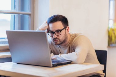 Adam dizüstü bilgisayarda çalışırken vurguladı. Hayal kırıklığına uğramış genç işadamı işyerinde elle başında oturan üzgün.