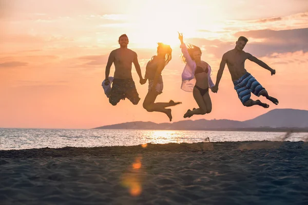 Group of happy people dancing and jumping inside sea on beautiful summer sunset