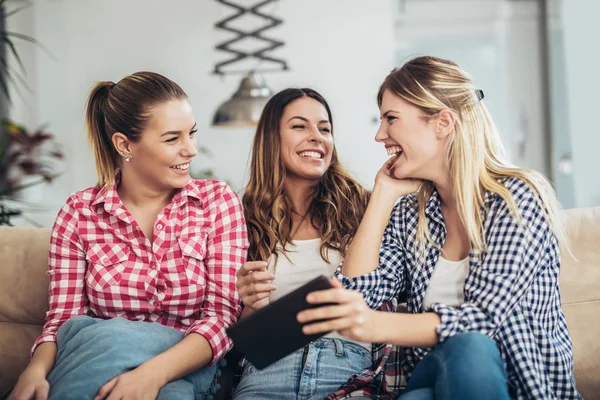 Three best friends using digital tablet together. Women sitting on sofa having fun surfing on the internet using smart digital pc tablet modern device