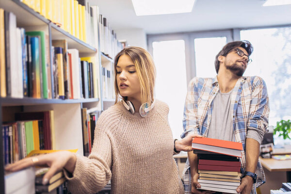 Girl searching for books in library and guy holding books