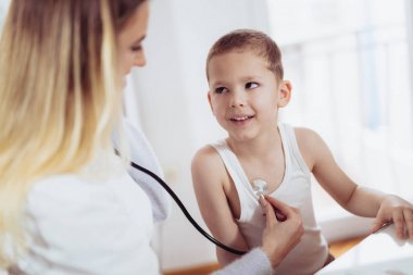 Doctor examining a little boy by stethoscope, medicine, healthcare, pediatric and people concept clipart