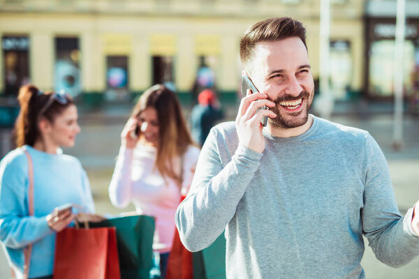 Happy friends shopping. Young friends enjoying shopping in the city. Man using phone.