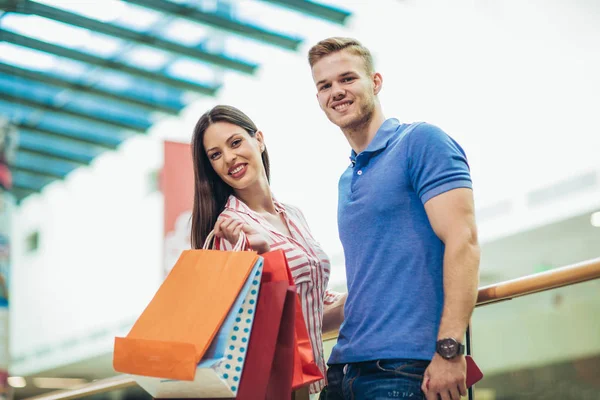 幸せな美しい若いカップル ショッピング バッグを押しながらモールで笑みを浮かべて — ストック写真
