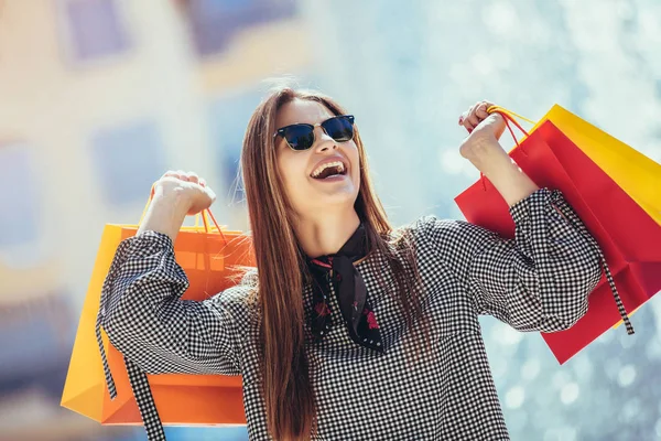 Menina Bonita Óculos Sol Segurando Sacos Compras Sorrindo Enquanto Caminha — Fotografia de Stock