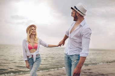 Kumsalda el ele tutuşan gülümseyen çift