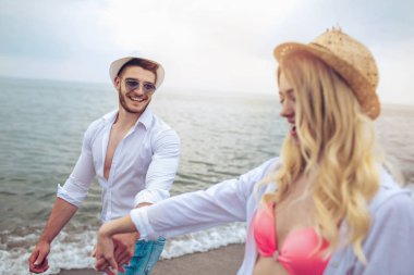 Kumsalda el ele tutuşan gülümseyen çift