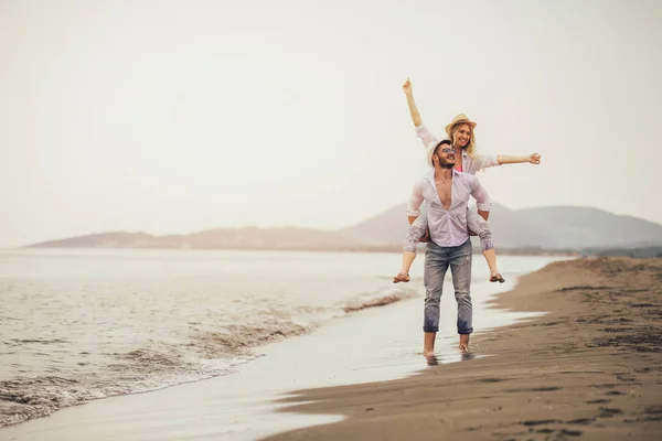 夏のビーチの休暇の愛に幸せなカップル うれしそうな女の子楽しんで若い彼氏にピギーバッ キング — ストック写真