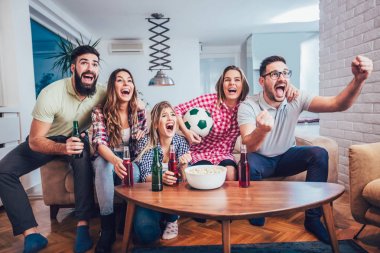 Mutlu arkadaşlar ya da futbol taraftarları televizyonda maç izleyip zaferi evde kutluyorlar. Dostluk, spor ve eğlence kavramı..