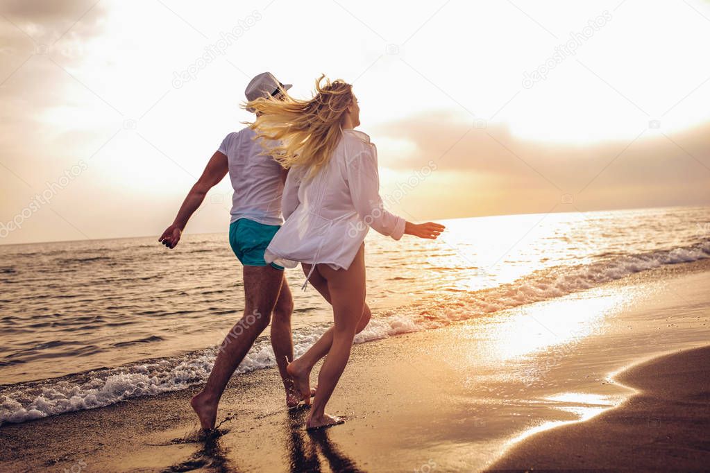 Rear view of happy couple running on beach at sunset.