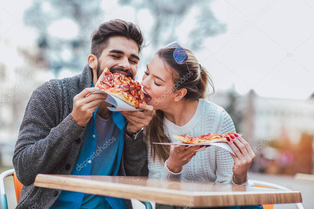Couple eating pizza outdoors and smiling.They are sharing pizza in cafe.