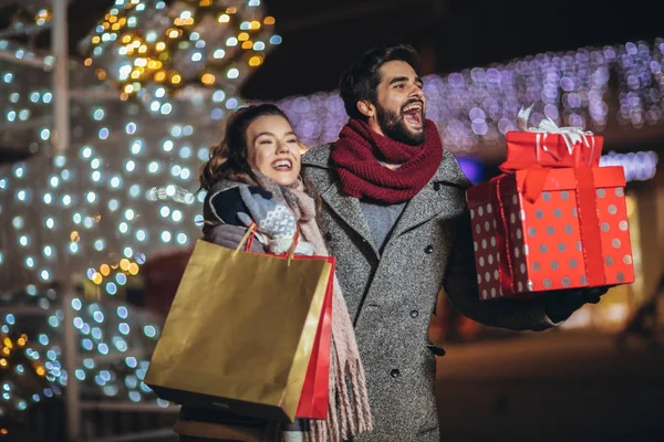 Casal com saco de presente no fundo luzes de Natal durante walki — Fotografia de Stock