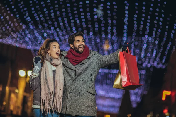 Casal com saco de presente no fundo luzes de Natal durante walki — Fotografia de Stock