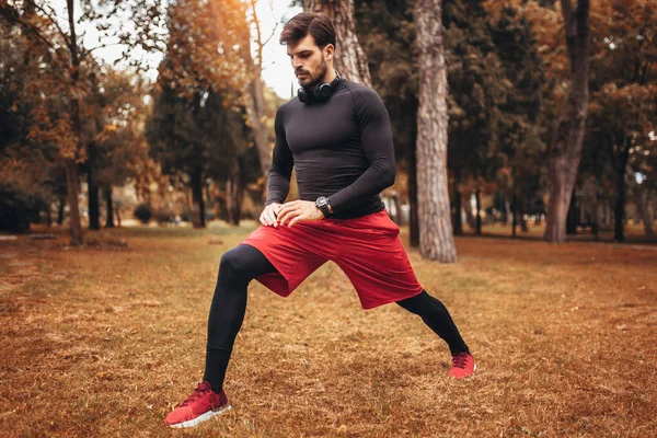 Esporte homem que se estende no parque de outono, fazendo exercícios . — Fotografia de Stock