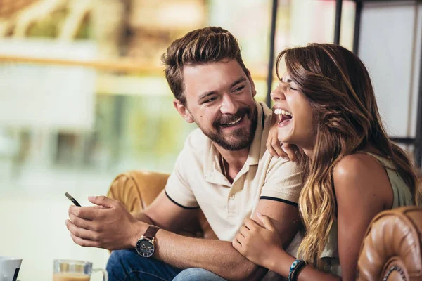 Beautiful young couple using a smartphone and smiling while sitt — Stock Photo, Image