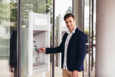 Genç iş adamı ATM kullanıyor. Kredi kartıyla para çekmiş.