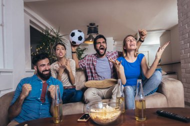 Arkadaşlar evde, evde futbol maçı izleyerek eğleniyorlar..