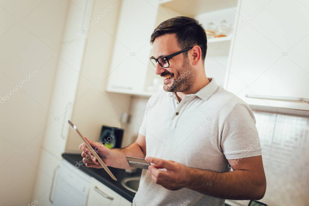 Smiling man with tablet pc and credit card at home