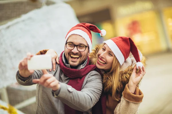 Joven hermosa pareja con sombreros de Santa hacer foto selfie en el —  Fotos de Stock