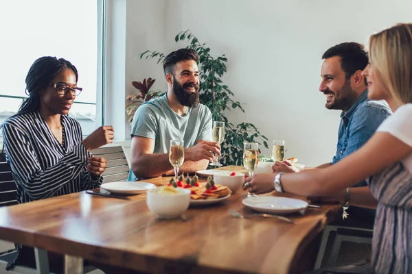 Fröhliche junge Leute genießen das Essen, während sie am Esstisch sitzen — Stockfoto