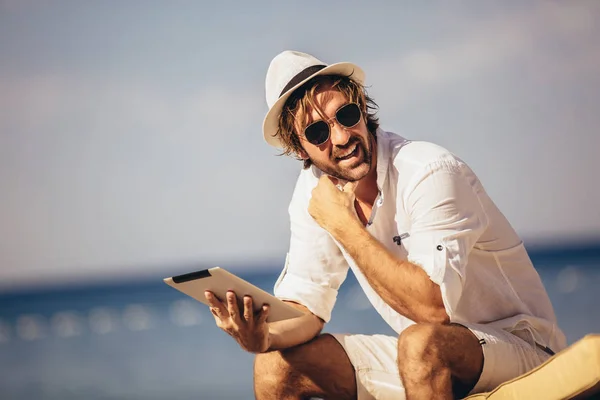 Человек расслабляется и пользуется планшетным компьютером на морском пляже — стоковое фото