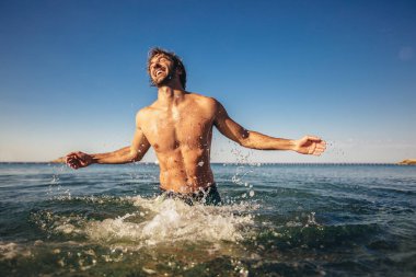 Deniz kenarında poz veren yakışıklı genç adam.