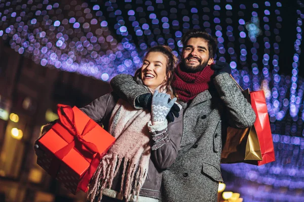 Paar mit Geschenktüte auf Weihnachtsbeleuchtung Hintergrund während walki — Stockfoto