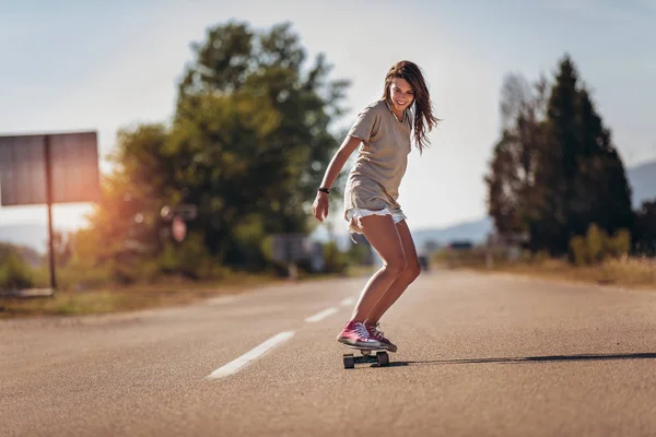 Jonge sportieve vrouw rijden op het skateboard op de weg. — Stockfoto