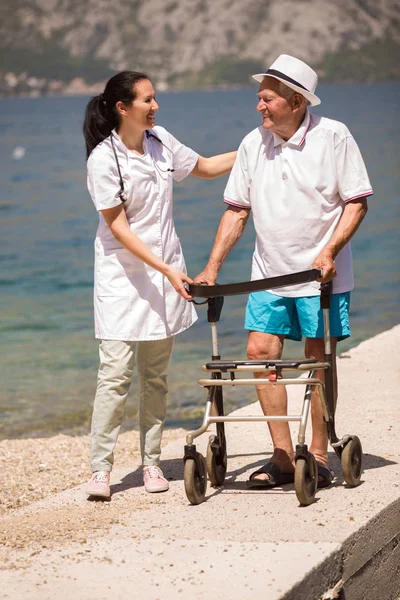 Verpleegkundige helpen oudere senior man. Senior man met behulp van een wandelaar met — Stockfoto