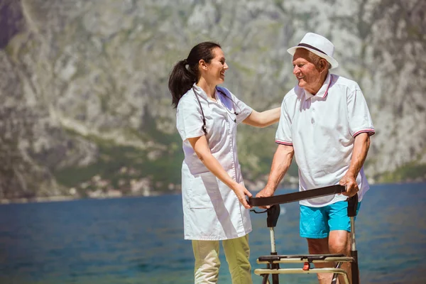 Sjuksköterska att hjälpa äldre senior man. Äldre man med en rullator med — Stockfoto