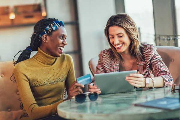 Två kvinnor som använder surfplatta och kreditkort tillsammans inne på caféet. — Stockfoto
