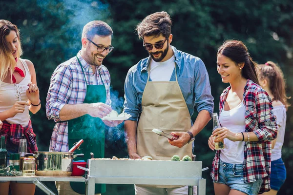 Freunde stehen am Grill, einer kocht am Grill — Stockfoto