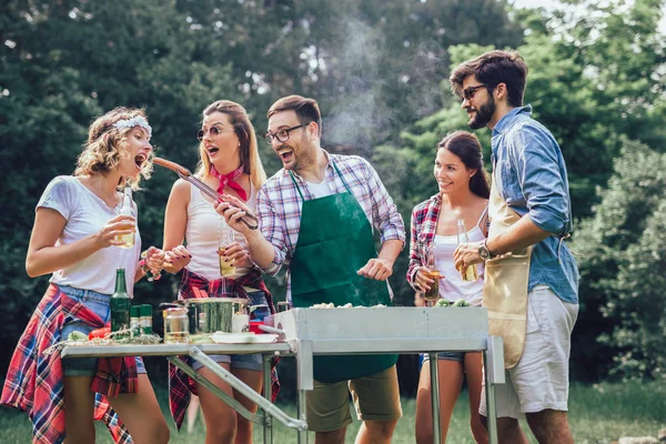 Группа друзей стоит на барбекю, одна готовит на гриле — стоковое фото