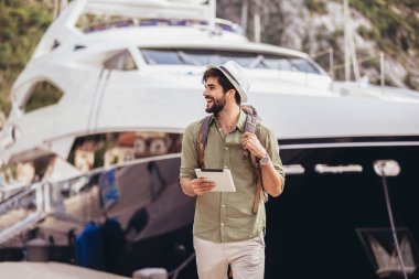 Genç bir adam B ile turistik bir tatil köyünün limanında yürüyor.