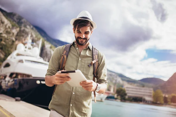 Young man walking by the harbor of a touristic sea resort with b