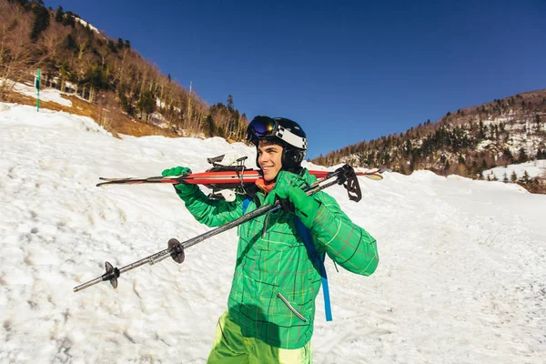 Młody mężczyzna trzyma narty, odwraca wzrok i uśmiecha się. — Zdjęcie stockowe