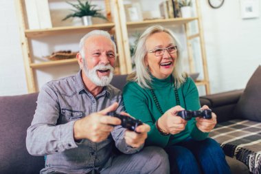 Senior couple having fun at home playing video game holding joys