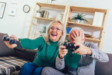 Senior couple having fun at home playing video game holding joys