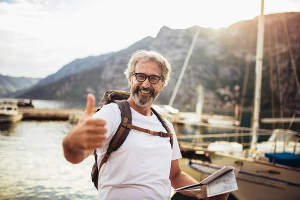 Sorridente turista maturo uomo in piedi con mappa e zaino vicino t — Foto Stock