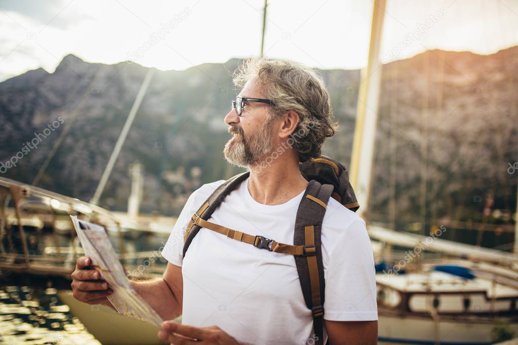 Smiling tourist mature man standing with map and backpack near t