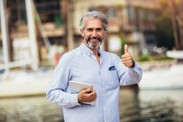 Uomo anziano che tiene tablet digitale sul porto turistico . — Foto Stock