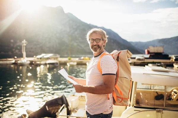 Sorridente turista maturo uomo in piedi con mappa e zaino vicino t — Foto Stock