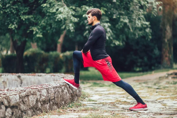 Młody sportowiec rozciągający się w parku, ćwiczący. — Zdjęcie stockowe