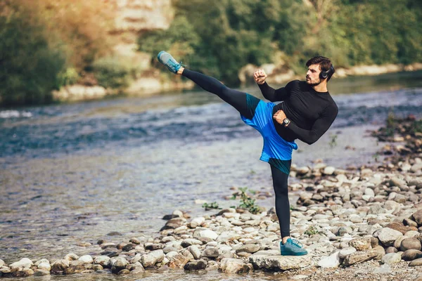 Handsome young man stretching on river bank. — Stock Photo, Image