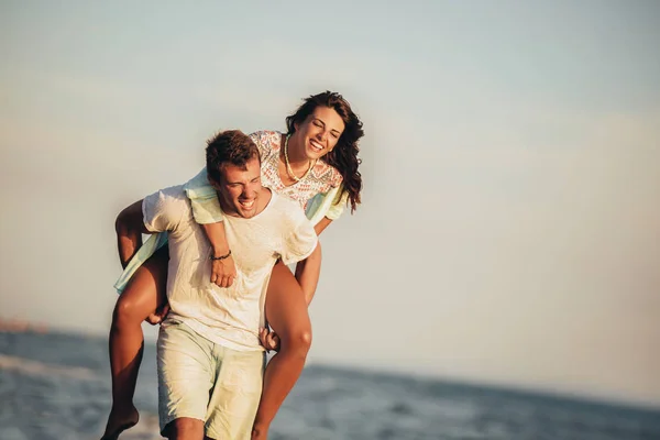 Bonito jovem dando passeio de piggyback para namorada na praia . — Fotografia de Stock