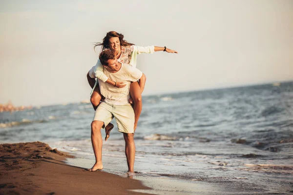 Bonito jovem dando passeio de piggyback para namorada na praia . — Fotografia de Stock