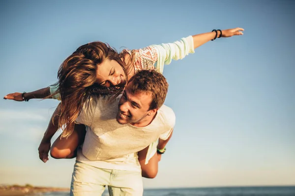 Bonito jovem dando passeio de piggyback para namorada na praia . — Fotografia de Stock